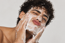 Jeune homme aux cheveux bouclés qui se nettoie le visage avec une mousse blanche