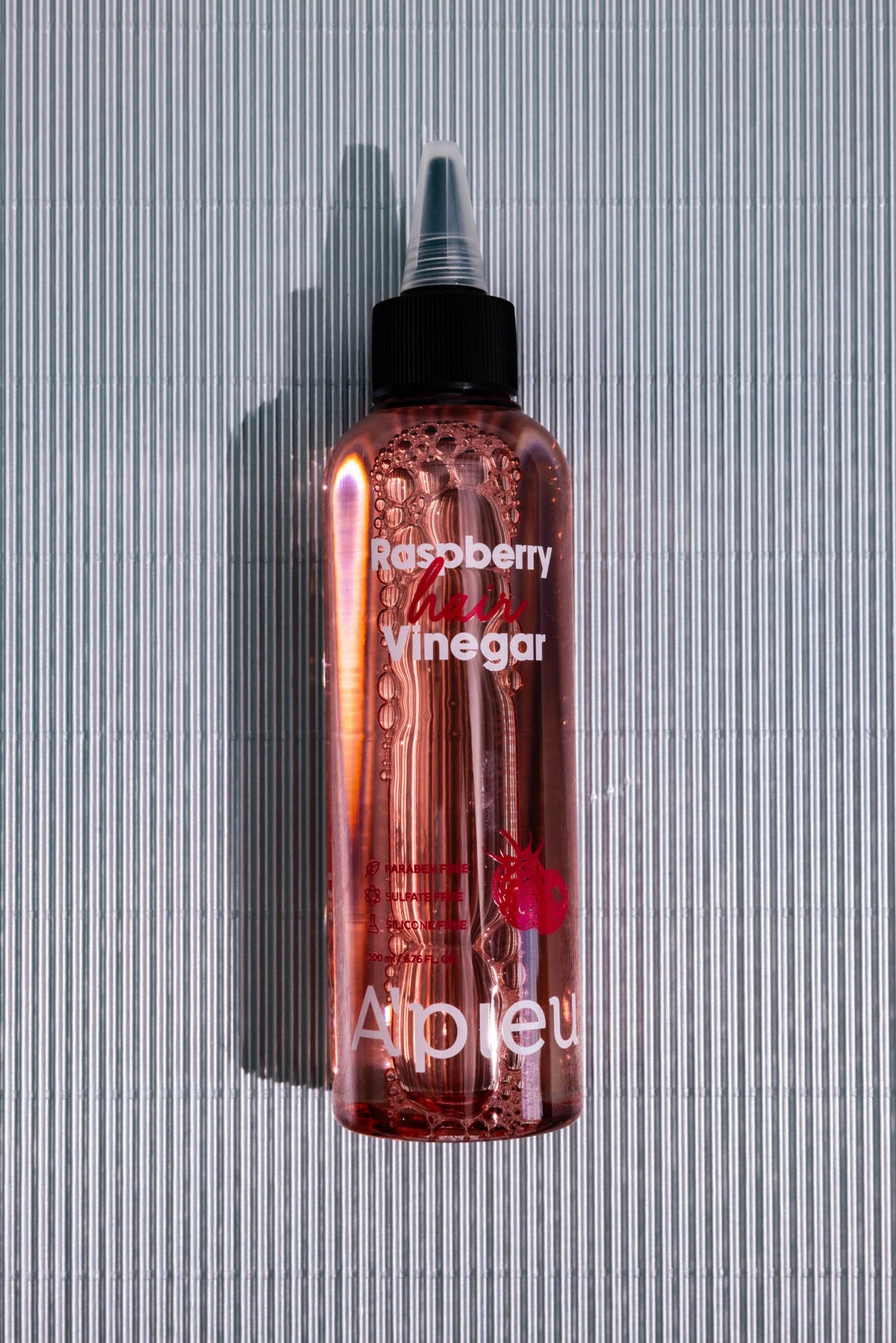 Vinaigre cuir chevelu Raspberry Hair Vinegar A’PIEU, flacon à embout verseur sur fond gris strié