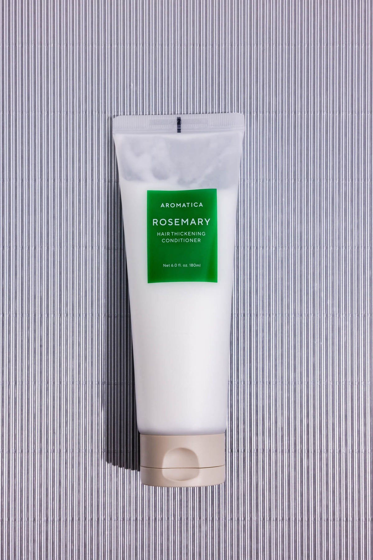 Après-shampoing Rosemary Hair Thickening Aromatica, tube posé à plat sur fond rayé gris