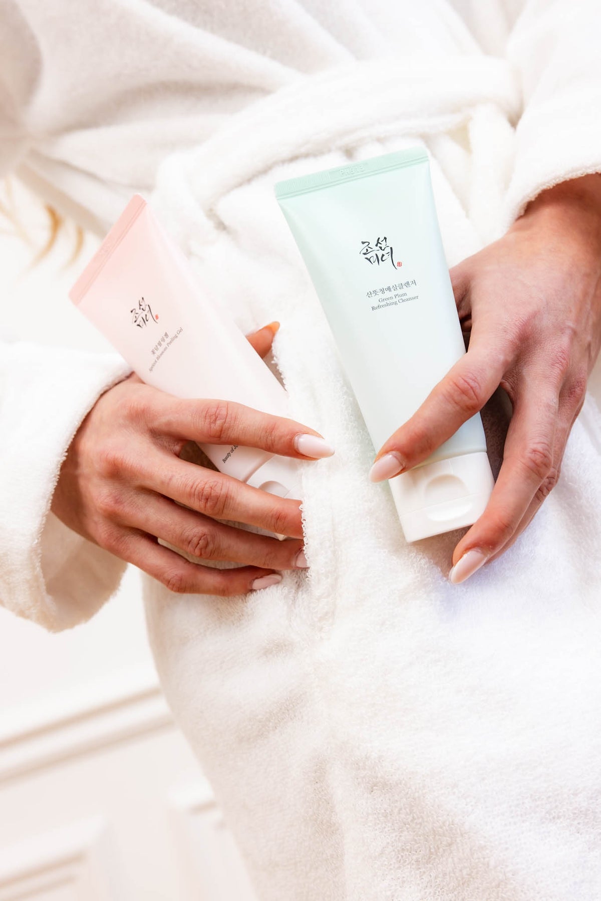Gel exfoliant Apricot Blossom Peeling Gel Beauty of Joseon, mannequin en peignoir tenant le tube rose et un tube vert