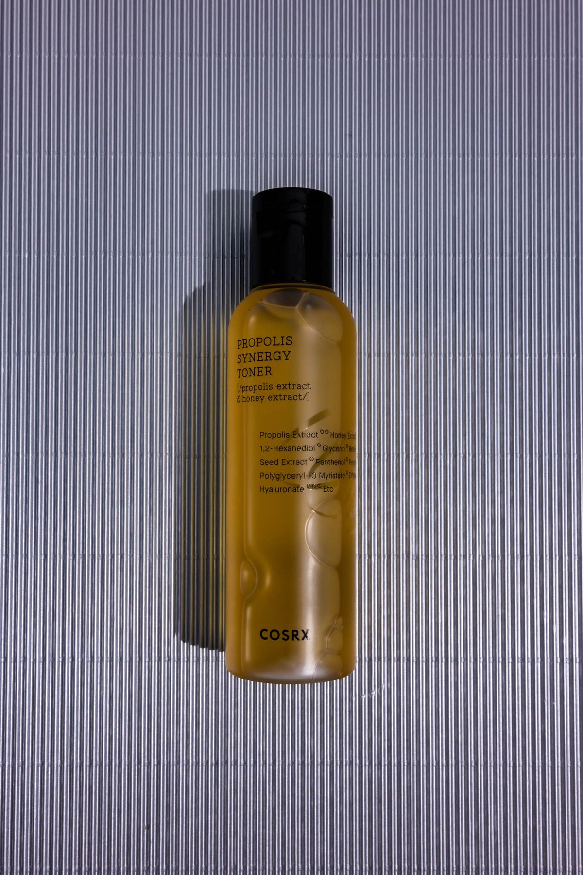 Lotion tonique Full Fit Propolis Synergy COSRX, flacon ambré posé sur fond strié gris, vue de dessus