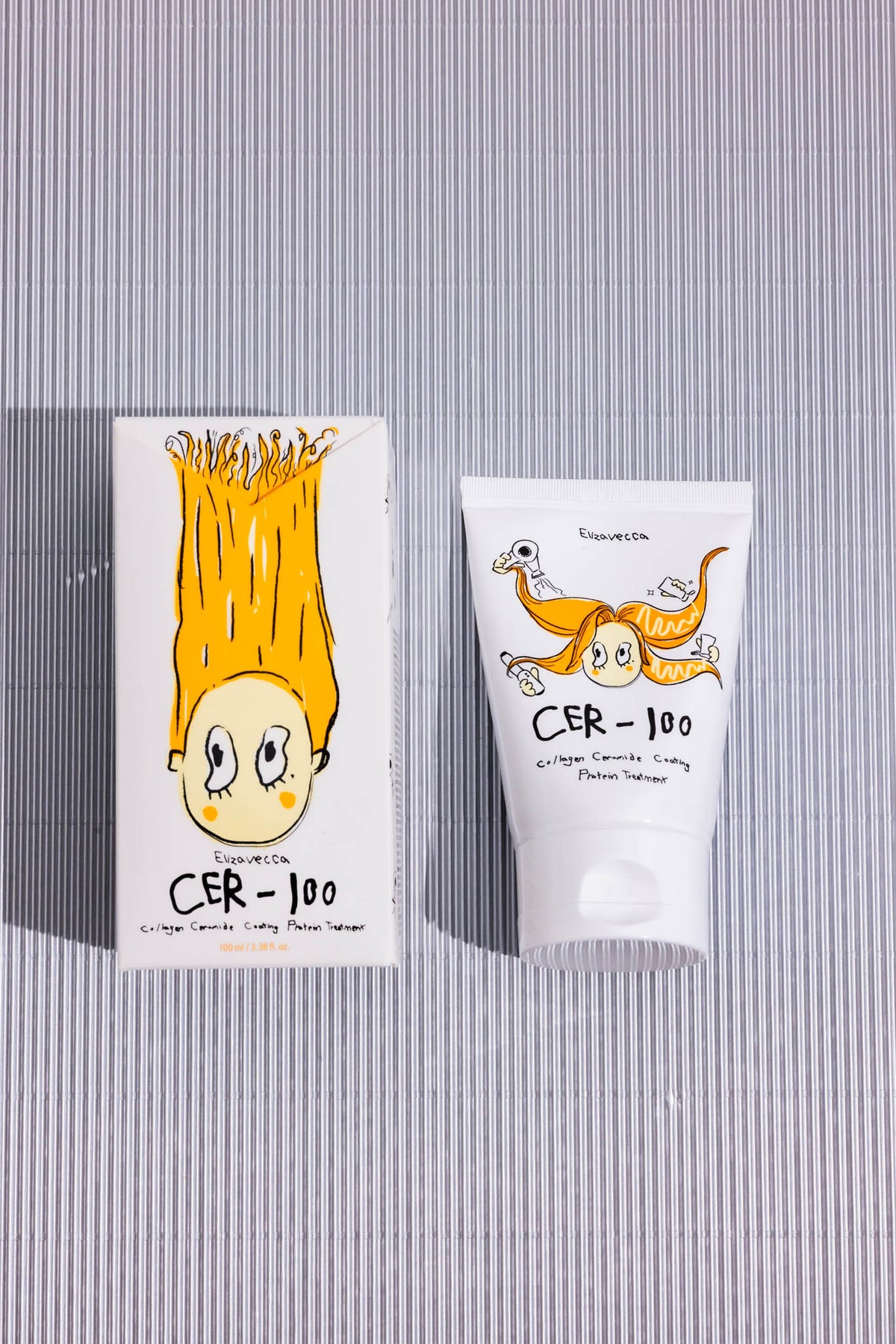 Soin cheveux Milky Piggy Cer-100 Collagen Ceramide Elizavecca, tube et boîte vus de dessus sur fond rayé gris