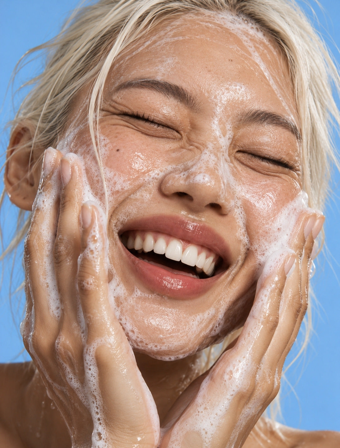 Un visage souriant couvert de mousse nettoyante, sur fond bleu
