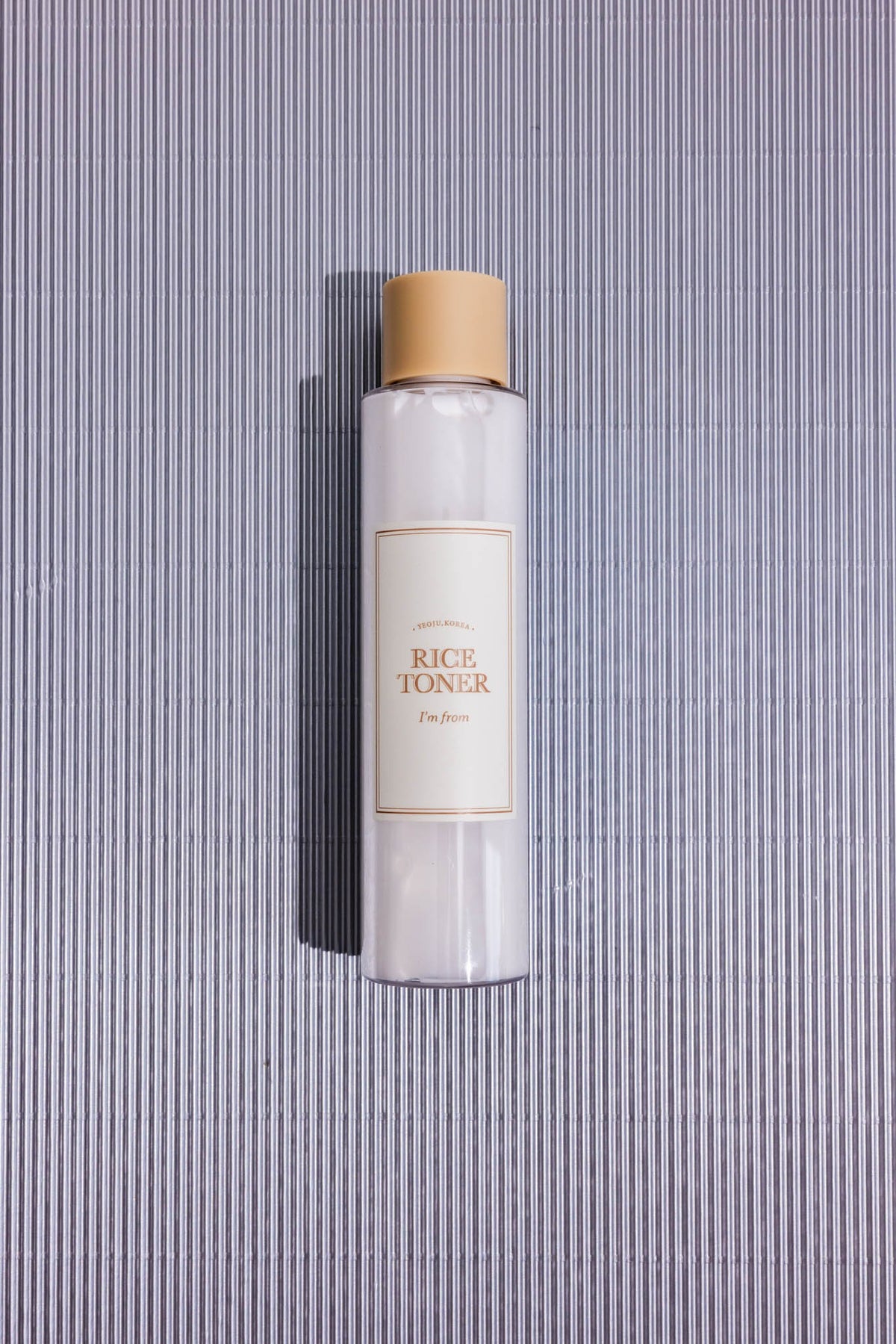 Lotion tonique hydratante au riz Rice Toner I’m from, flacon posé à plat sur fond rayé gris