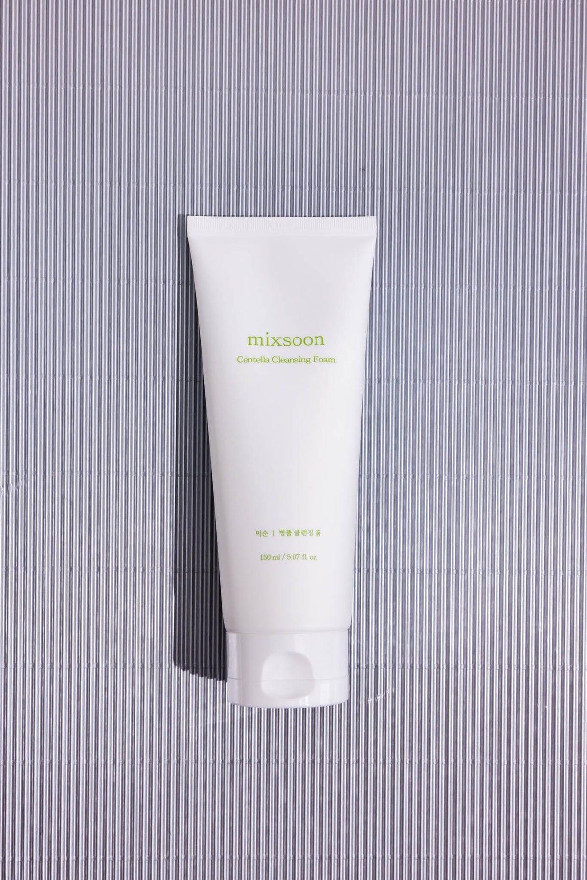 Mousse nettoyante douce à la centella Mixsoon, tube vu de dessus sur fond rayé gris