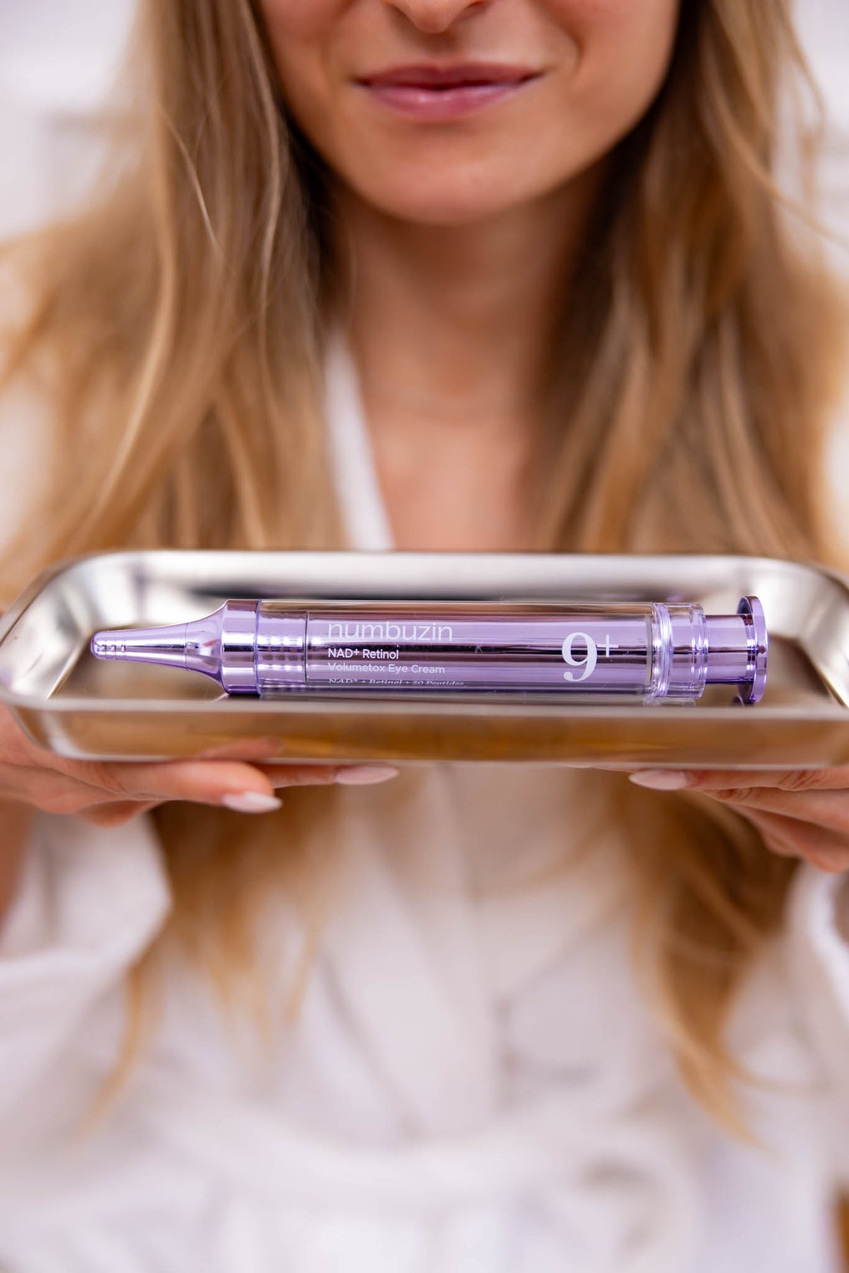 Crème yeux No.9 NAD+ Retinol Volumetox Numbuzin, tube seringue sur un plateau argenté tenu par une mannequin