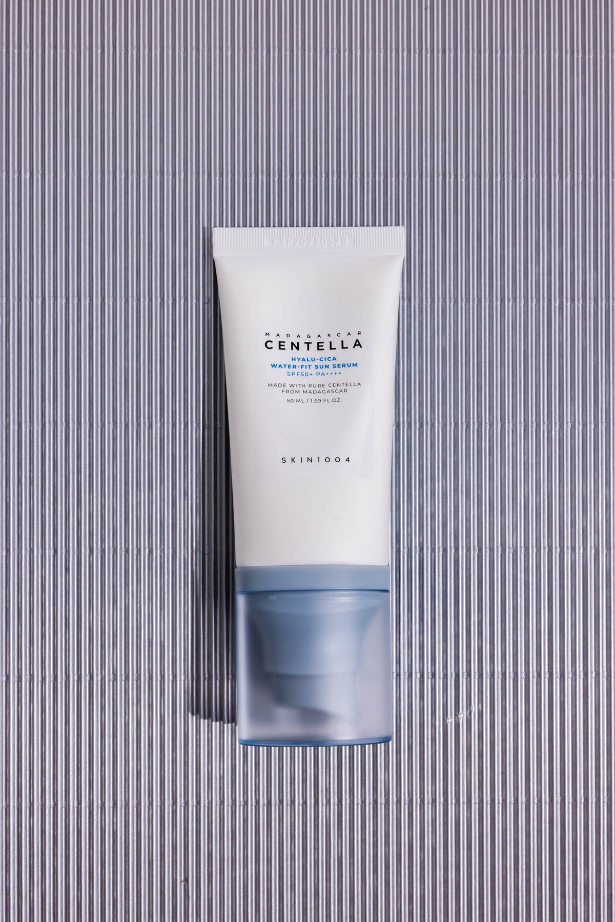 Sérum solaire Madagascar Centella Hyalu-Cica Water-Fit SKIN1004, tube posé sur fond strié gris, vue de dessus