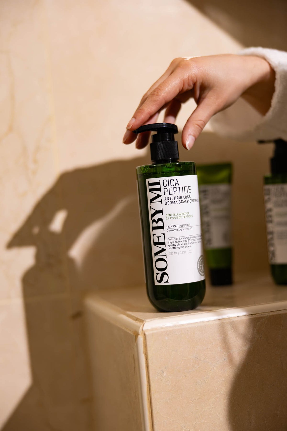 Shampoing Cica Peptide Anti Hair Loss Derma Scalp SOME BY MI, main actionnant la pompe du flacon posé sur un rebord
