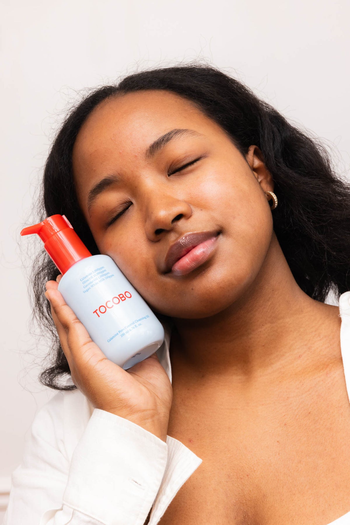Huile démaquillante Calamine Pore Control TOCOBO, mannequin yeux fermés tenant le flacon contre la joue