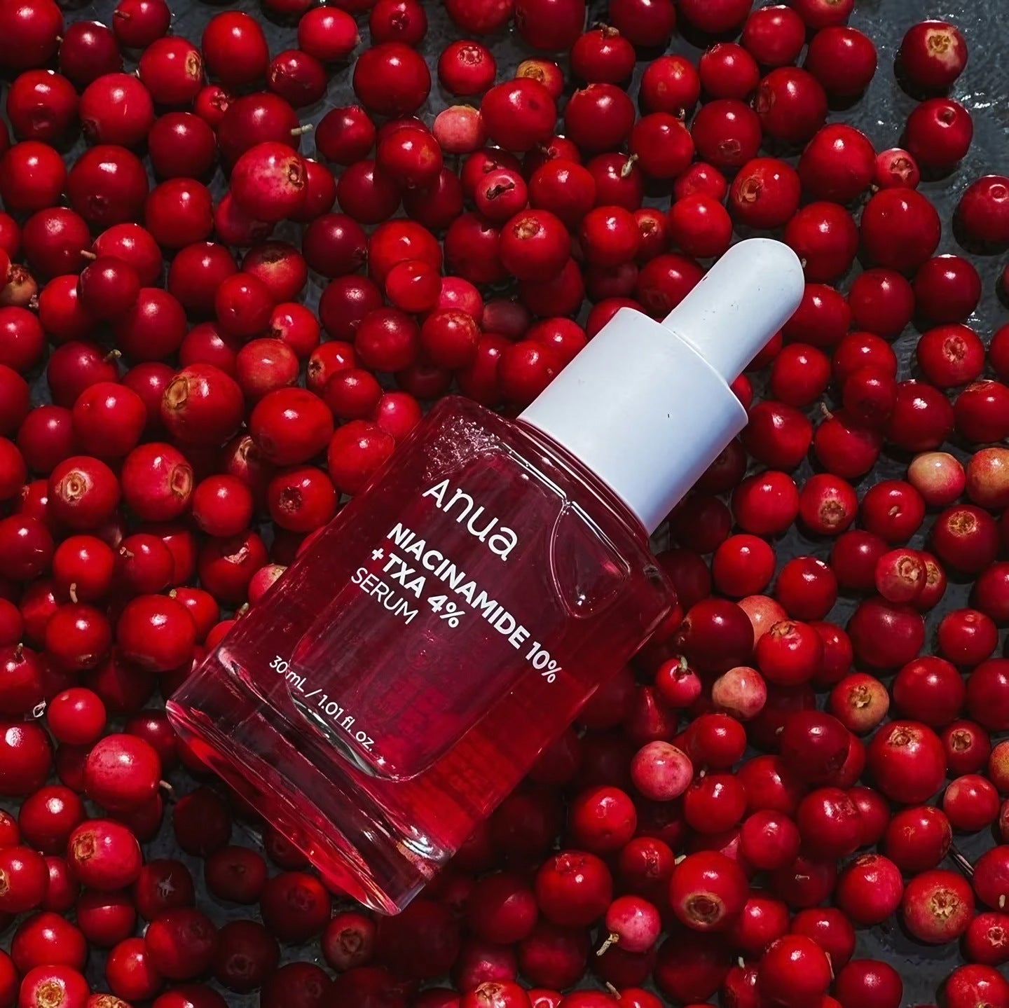 Anua, flacon du sérum Niacinamide 10 % + TXA 4 % posé sur un lit de canneberges