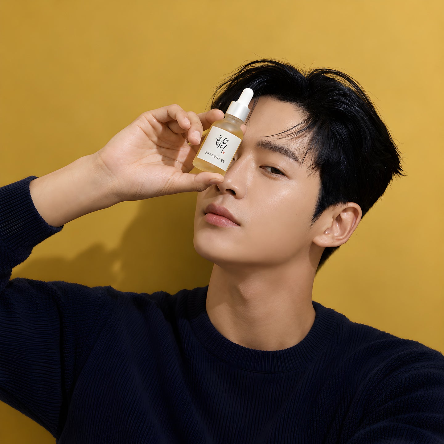 Beauty of Joseon, jeune homme tenant un flacon compte-gouttes devant l’œil, sur fond moutarde