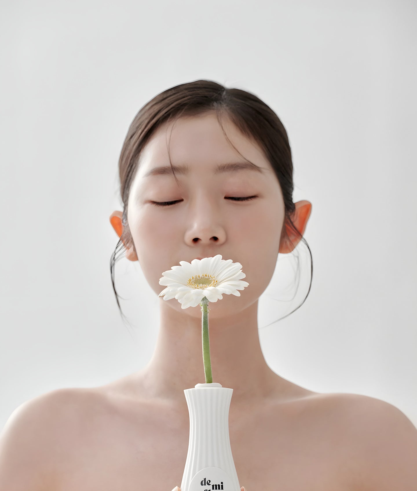 De Mi Flor, jeune femme aux yeux fermés, une marguerite dans un vase blanc devant la bouche