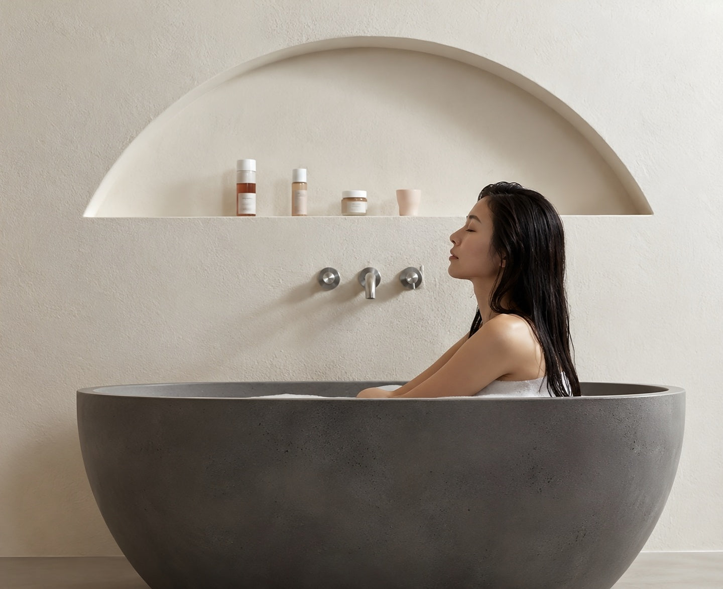Dr Ceuracle, une femme se détend dans une baignoire en pierre, ses soins posés sur l’étagère