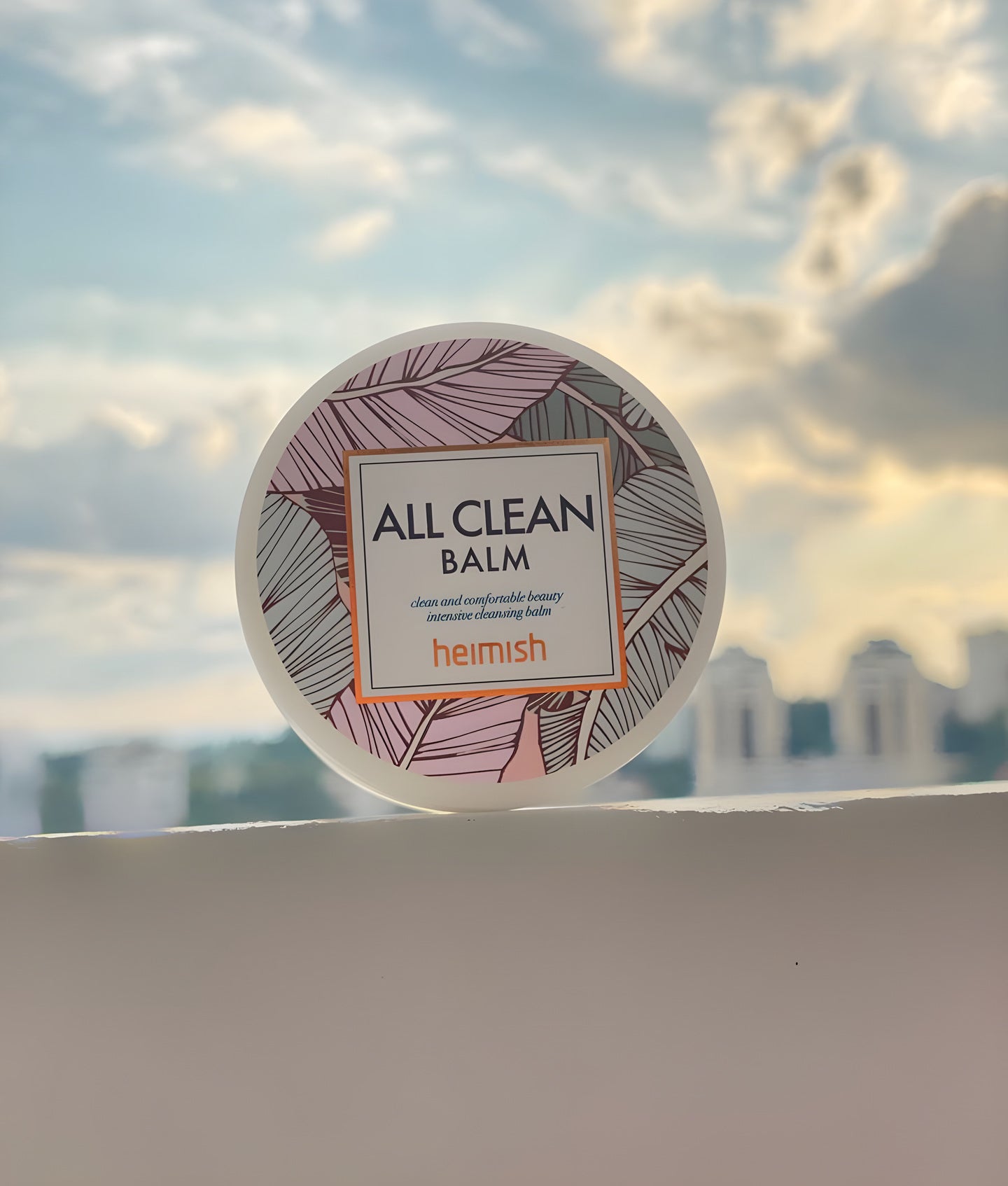 Heimish, pot de baume nettoyant All Clean Balm posé sur un rebord, devant un ciel nuageux