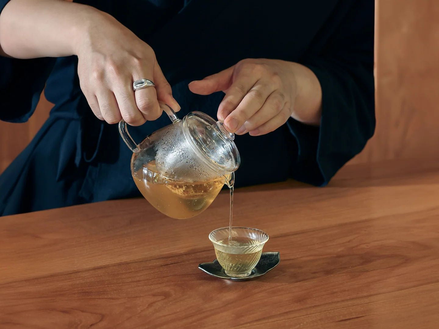 Pyunkang Yul, deux mains versent un thé doré d’une théière en verre dans une petite tasse